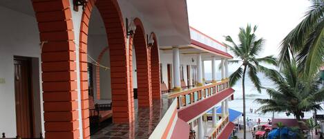 A hotel with a covered outdoor area featuring red brick arches, a tiled floor, and a view of the beach.