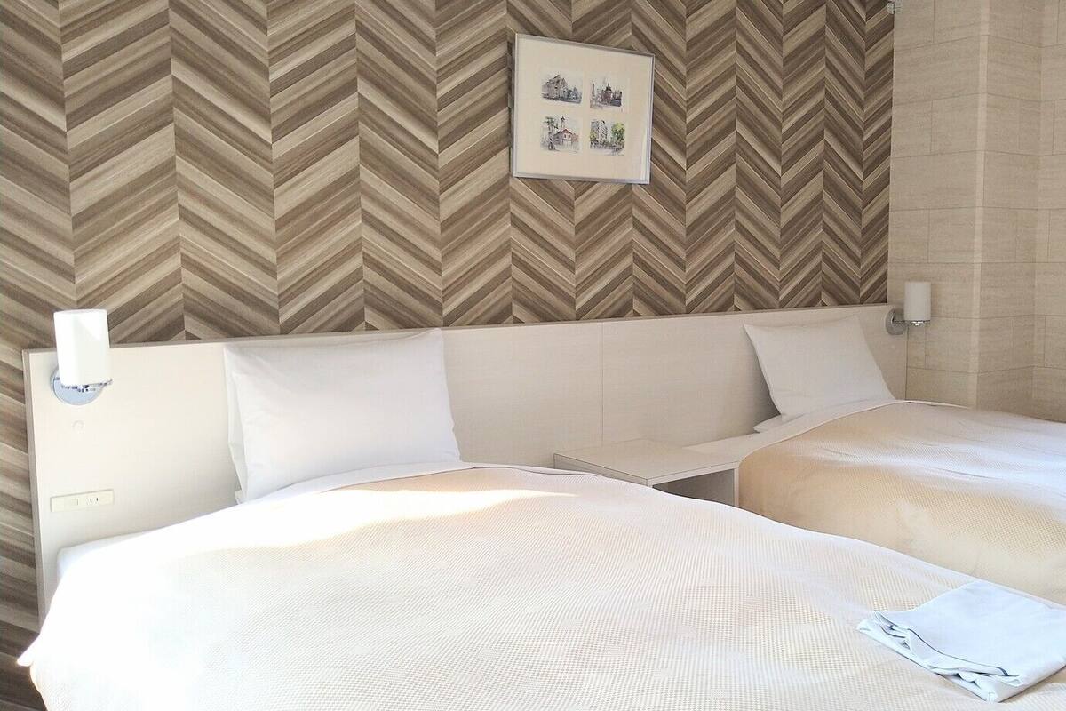 Une chambre d’hôtel avec deux lits, un mur orné d’un motif en chevrons, un tableau encadré et une lampe de chevet.
