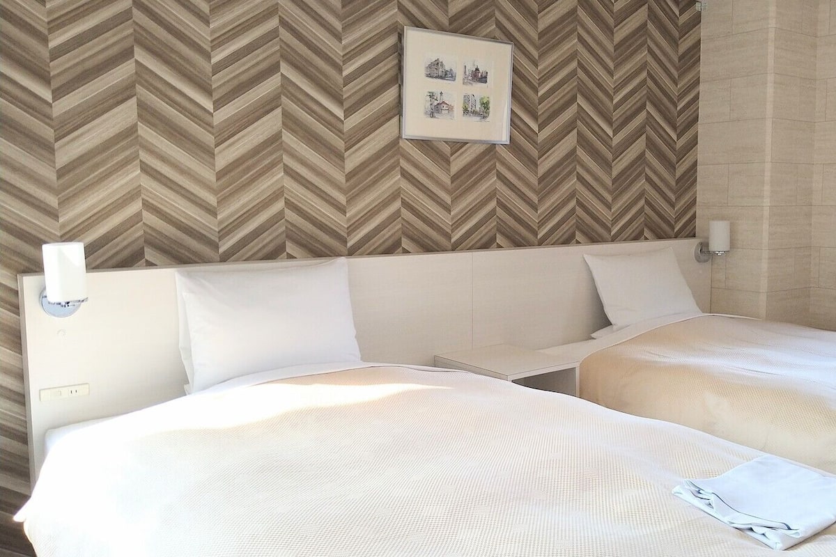 A hotel room with two beds, a chevron-patterned wall, a framed picture, and a bedside lamp.
