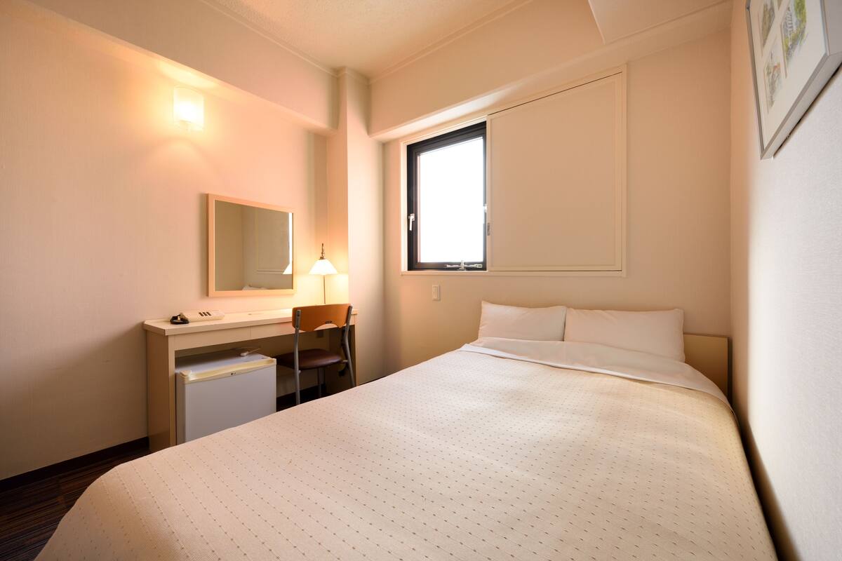 Une chambre d’hôtel équipée d’un lit, d’un bureau, d’une chaise et d’un petit réfrigérateur.