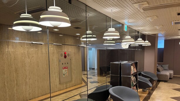 A modern waiting area with glass partitions, multiple seating options, and contemporary lighting fixtures.