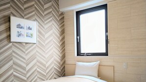 A bedroom with a herringbone-patterned wall, a window with a black frame, and a bed with a white headboard and pillow.