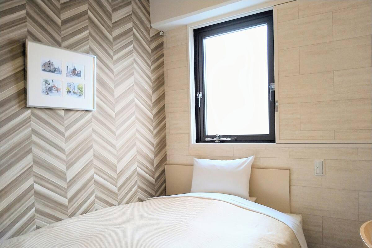 Une chambre avec un mur orné d’un motif en chevrons, une fenêtre à cadre noir et un lit doté d’une tête de lit et d’un oreiller blancs.