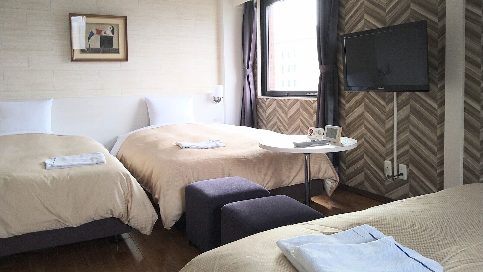 Una habitación de hotel con dos camas, una mesita con televisor, un televisor en la pared y un cuadro enmarcado.
