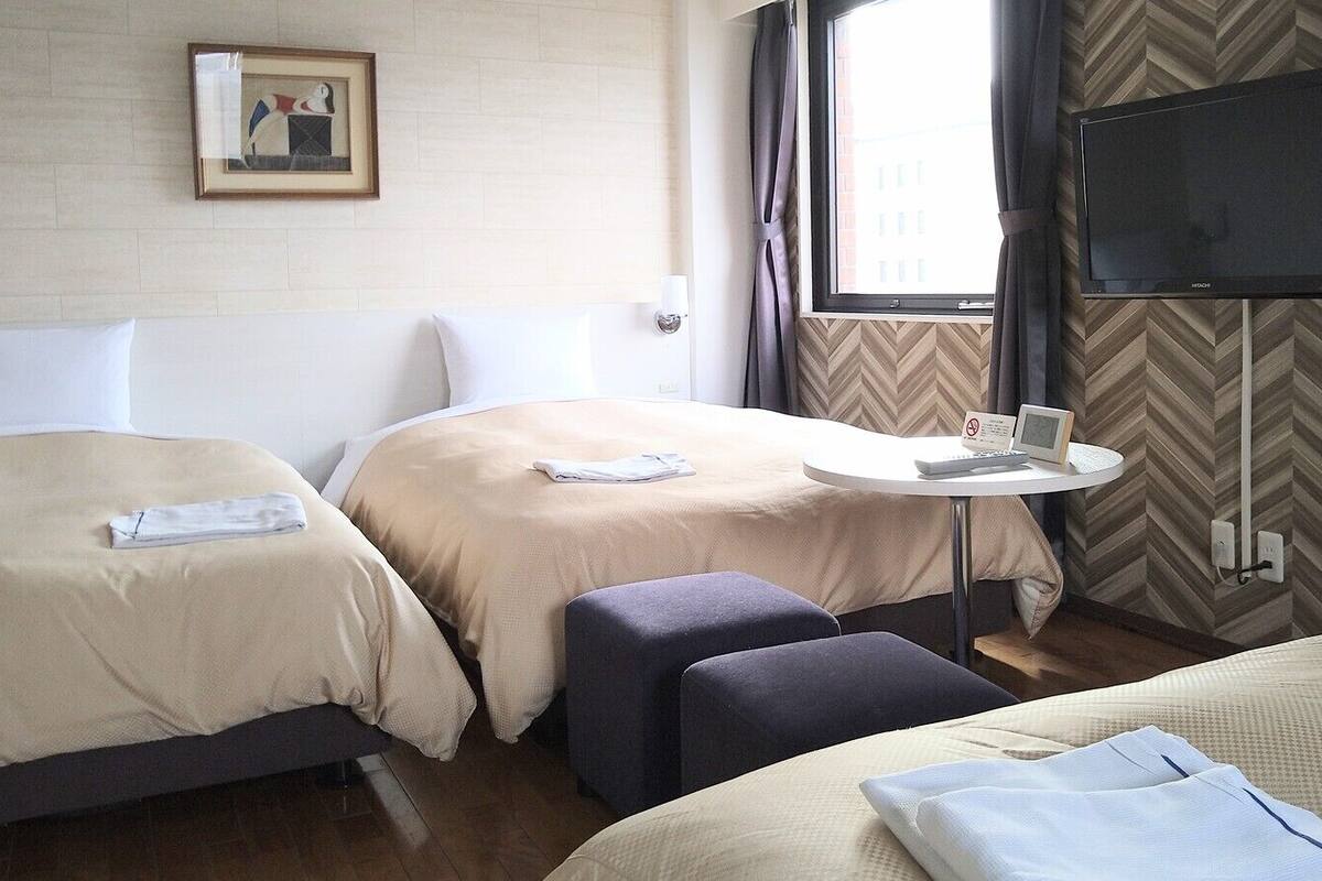 Une chambre d’hôtel avec deux lits, une petite table avec un téléviseur, un téléviseur fixé au mur et un tableau encadré.