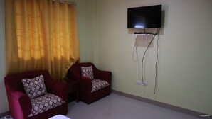 Una habitación con dos sillones rojos, un televisor montado en la pared y una cortina entreabierta.
