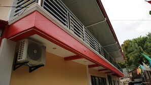 Un edificio con fachada roja y blanca, un balcón con barandilla de metal y una unidad de aire acondicionado instalada en la pared.