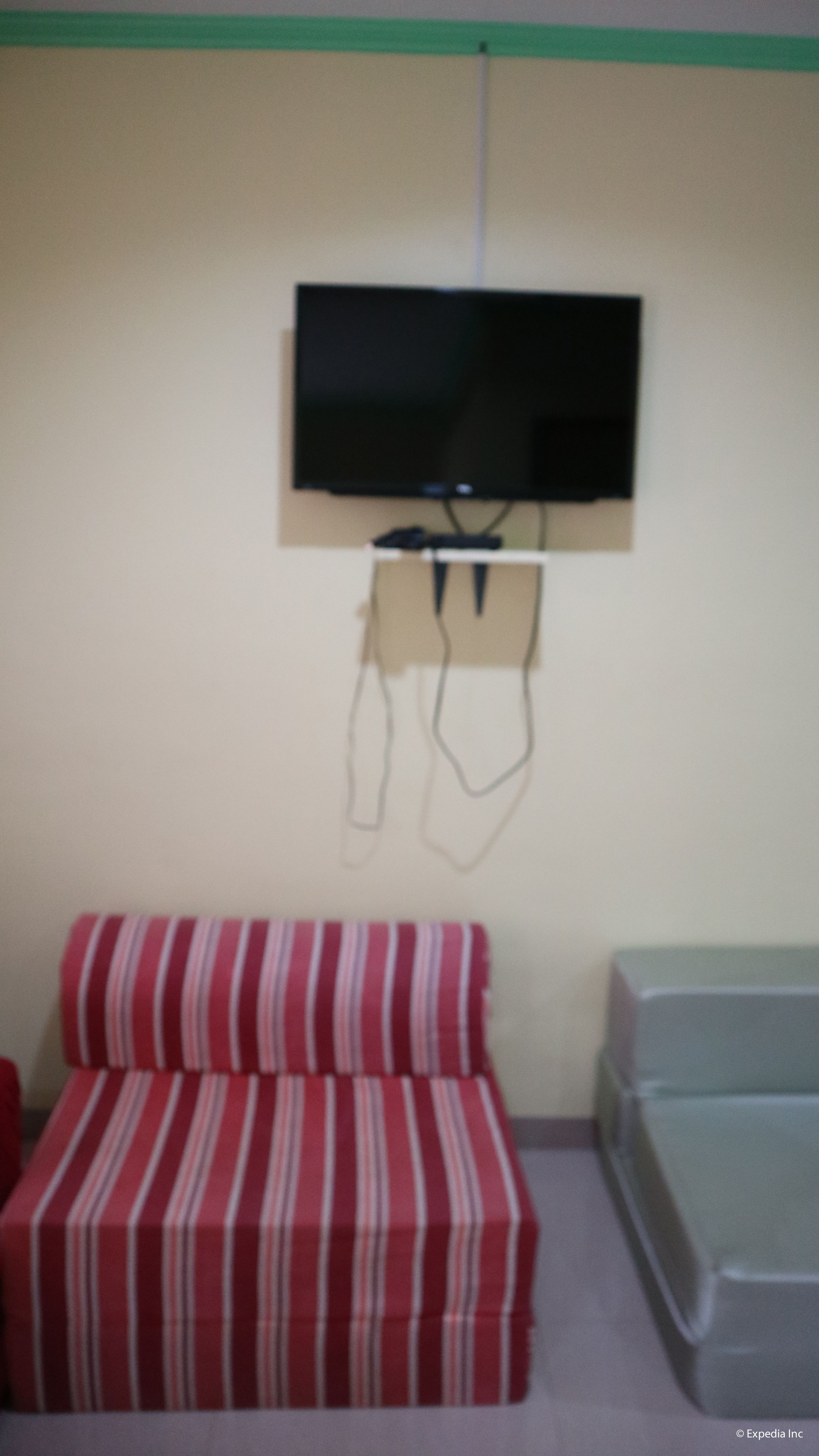 A room with a television mounted on the wall, a striped red sofa, and a bed with a grey mattress.