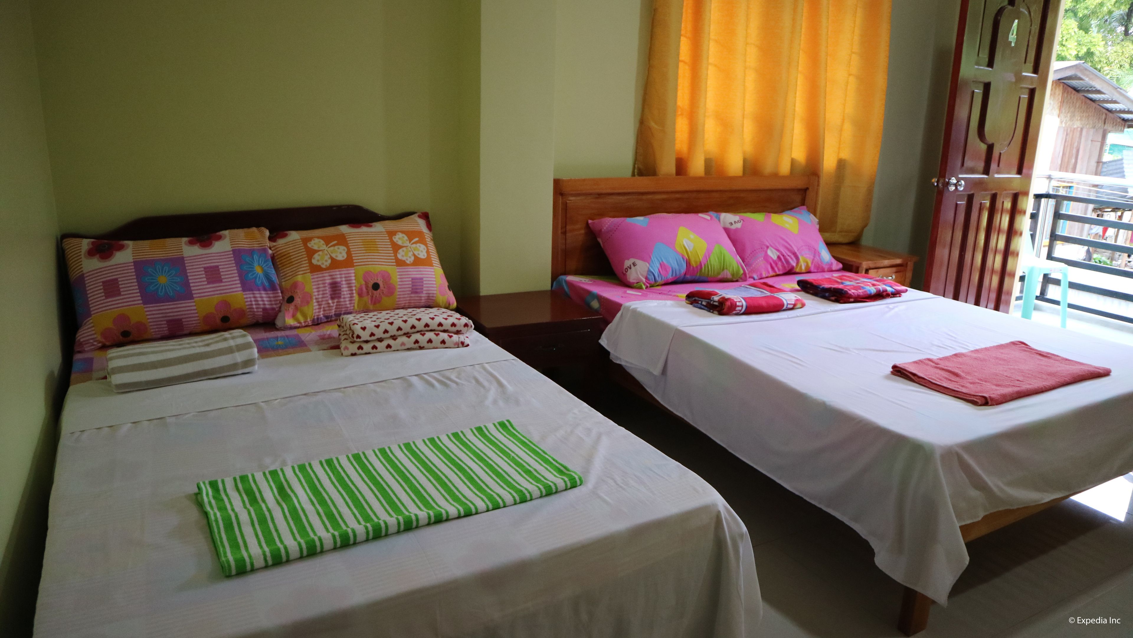 A hotel room with two beds, each with a different patterned bedspread. There are pillows with floral designs on one bed and a striped bedspread on the other.