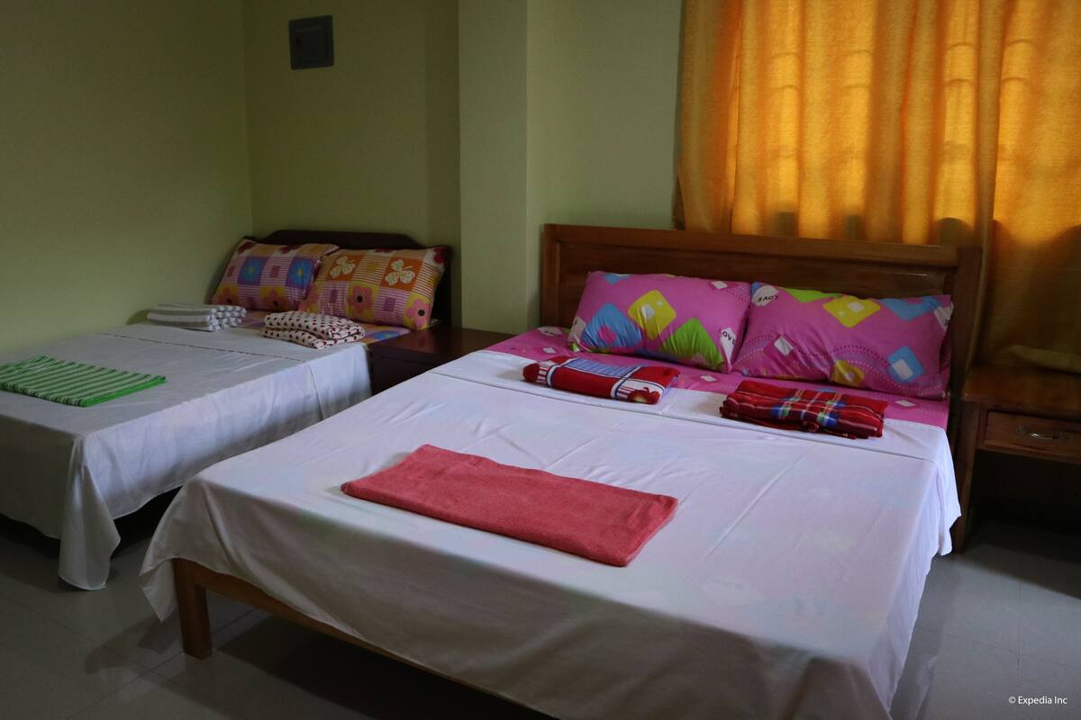 Two single beds with white linens, a wooden headboard, and colorful pillows.