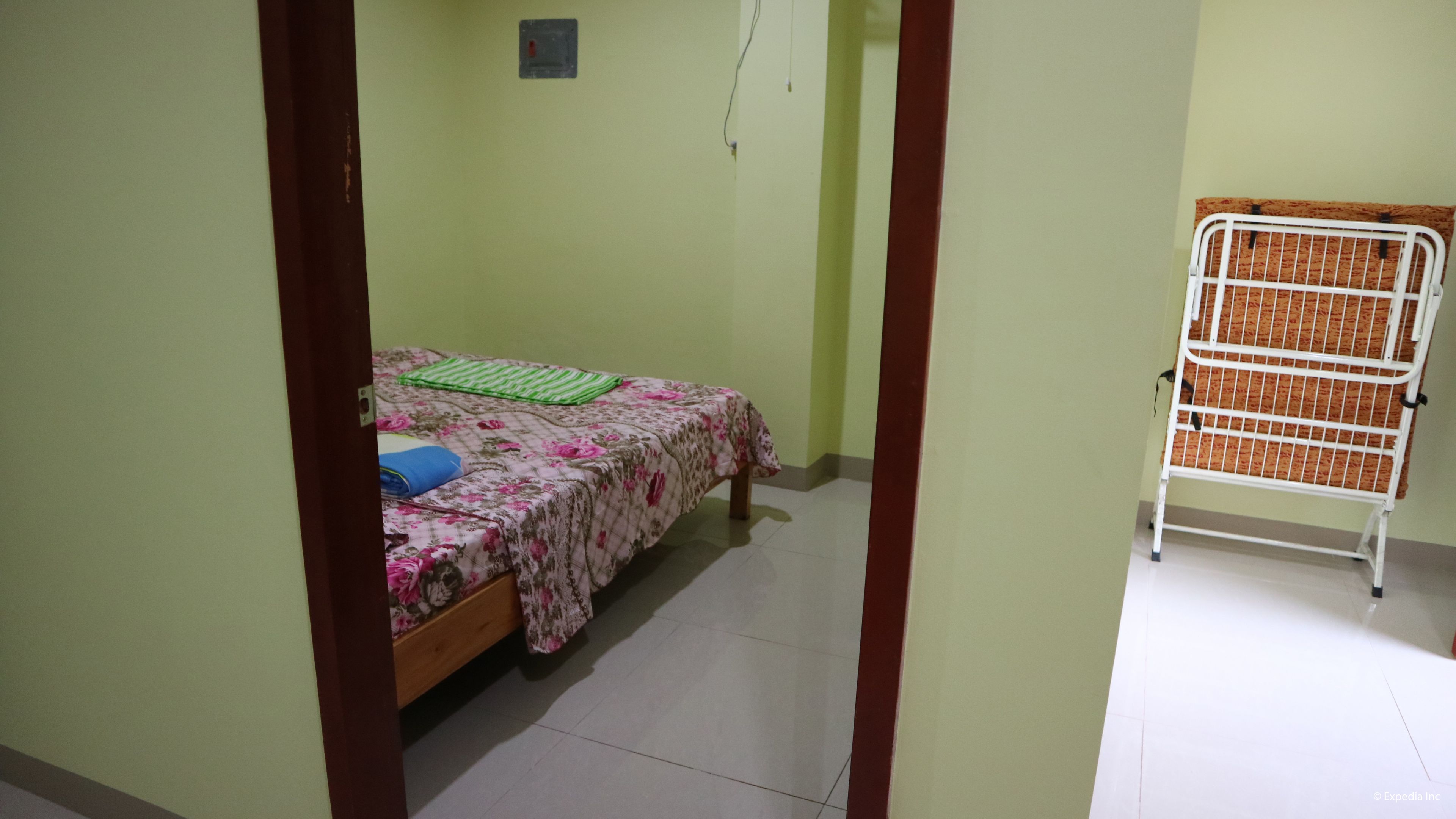 A small room with a bed, a metal rack, and a tiled floor.
