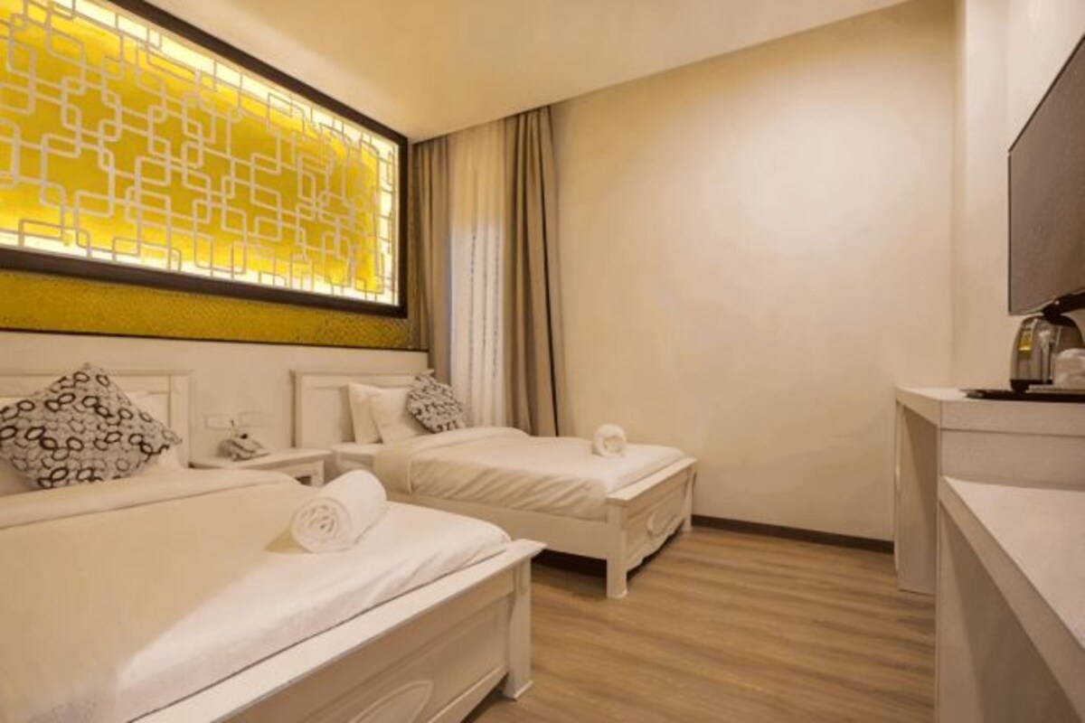 A hotel room with two beds, a large window with a geometric pattern, a flat-screen TV, and a wooden floor.