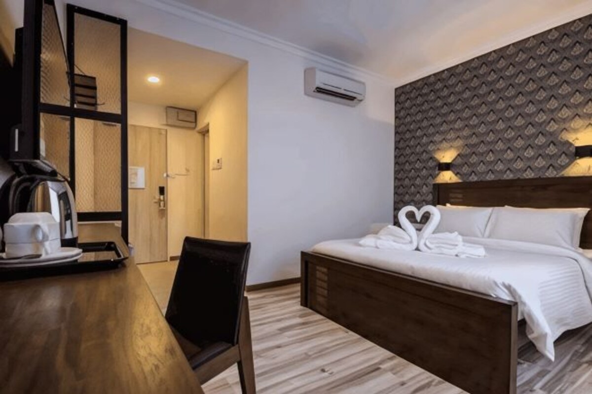 A hotel room with a bed, a desk with a coffee maker, a chair, and a wall-mounted air conditioner.