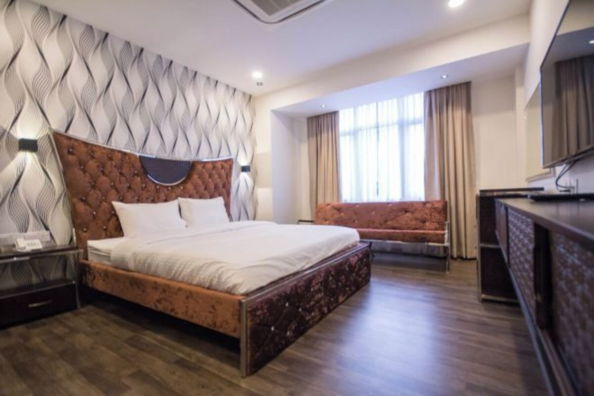 A modern hotel room with a large bed, a sofa, a TV, and a desk.