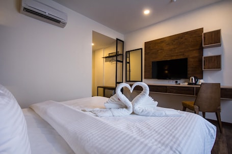 A hotel room with a neatly made bed, a TV, a desk with a coffee maker, and a mirror on the wall.