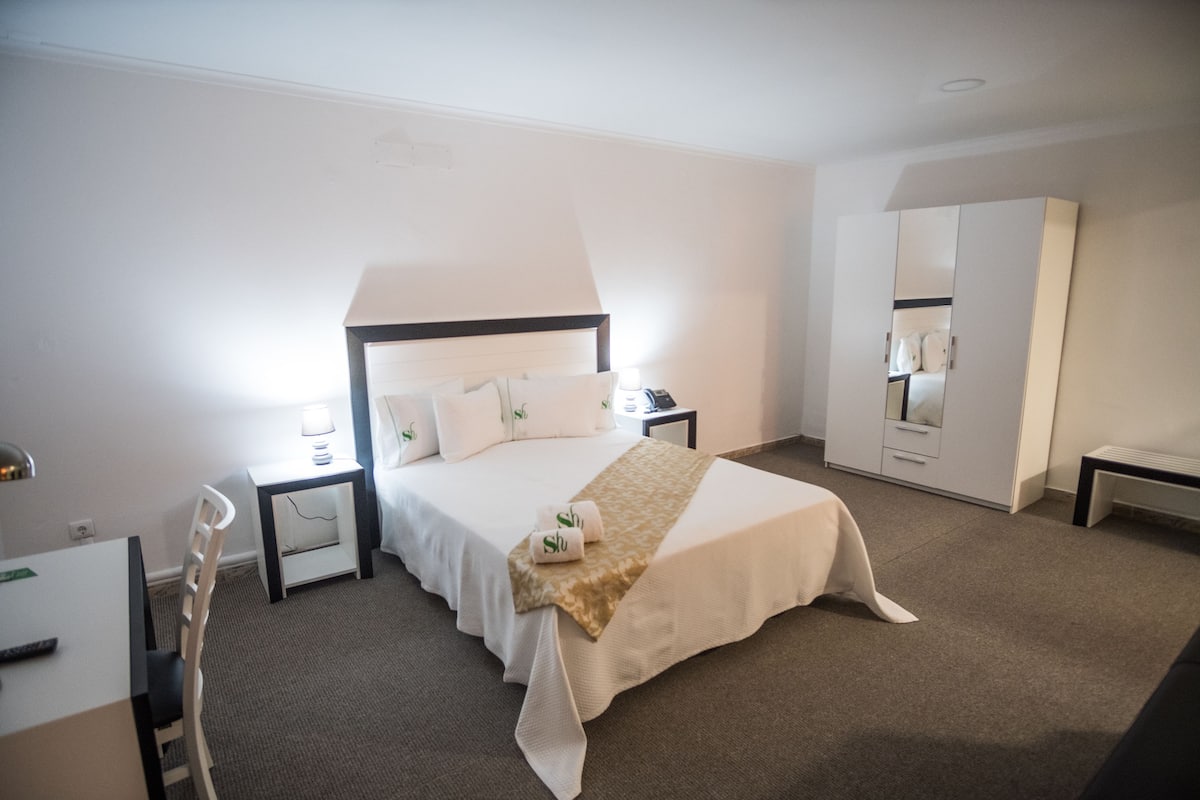 Een hotelkamer met een bed, nachtkastjes, een bureau en een kledingkast.