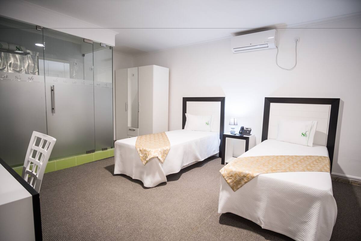 Een hotelkamer met twee eenpersoonsbedden, een bureau, een stoel, een kledingkast en een douchecabine met glazen wanden.