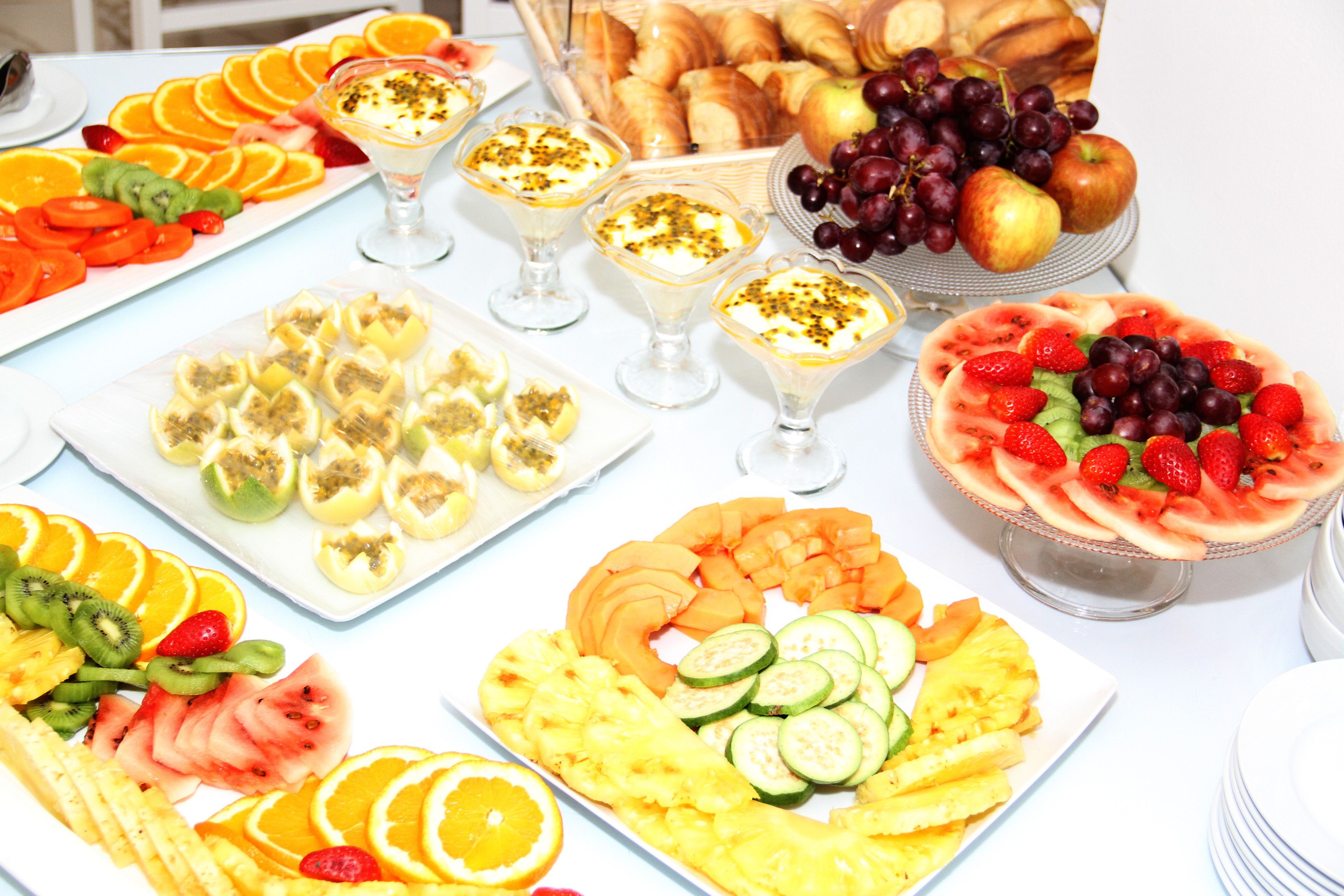 A table with various fruit platters, including sliced oranges, kiwi, and watermelon, and a basket of croissants.