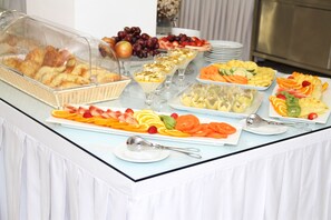 Una mesa de bufé con diversos alimentos, entre ellos frutas, pasteles y postres.