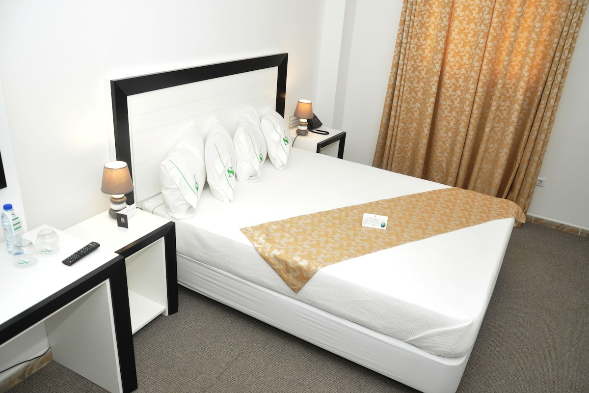 Een netjes opgemaakte hotelkamer met een bed, nachtkastjes, een lamp, een telefoon en een gordijn.