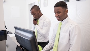 Deux hommes dans un cadre professionnel, l’un utilisant un ordinateur et l’autre au téléphone.