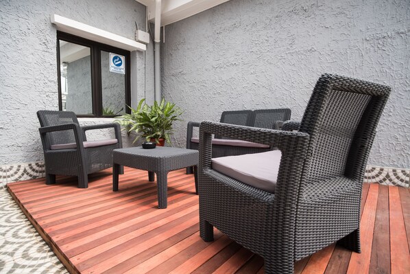 Un patio con mobiliario de mimbre, una mesita y una planta en maceta.