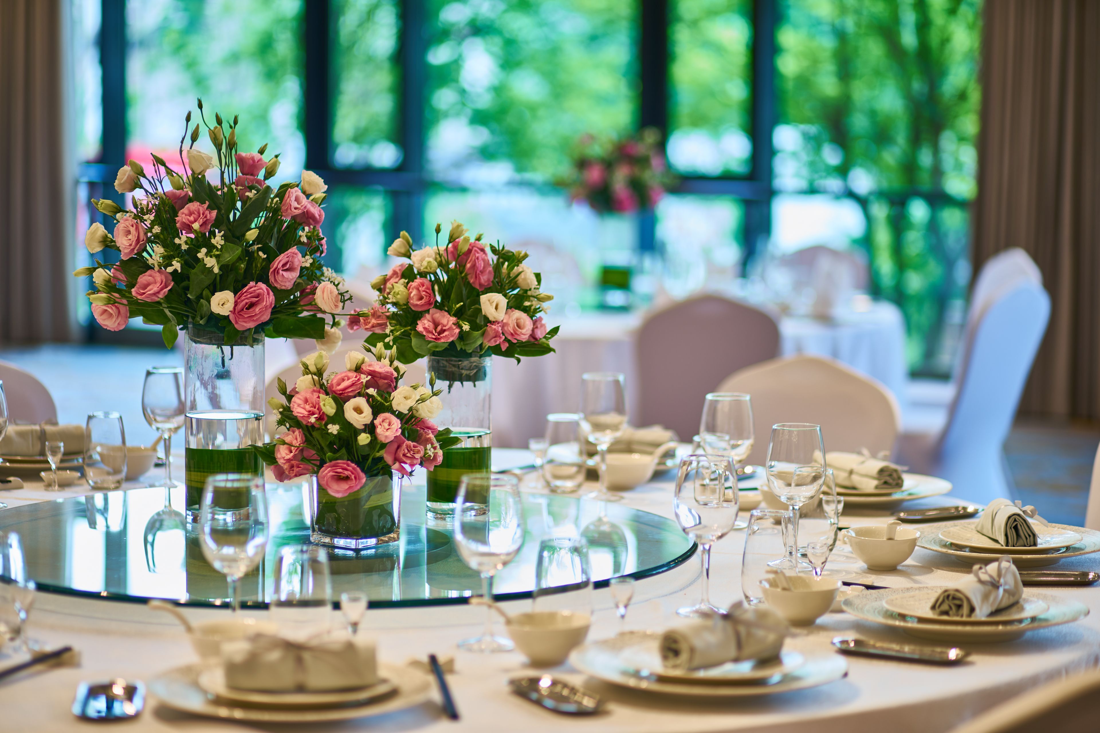 A round dining table with a glass top, surrounded by white chairs, set with plates, glasses, and cutlery.