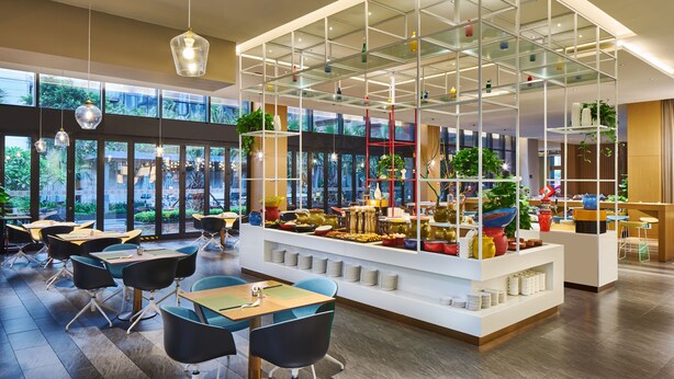 A modern dining area with tables and chairs, a central glass display, and large windows offering a view of greenery outside. - Days Hotel by Wyndham Haikou Meilan Airport (Haikou)