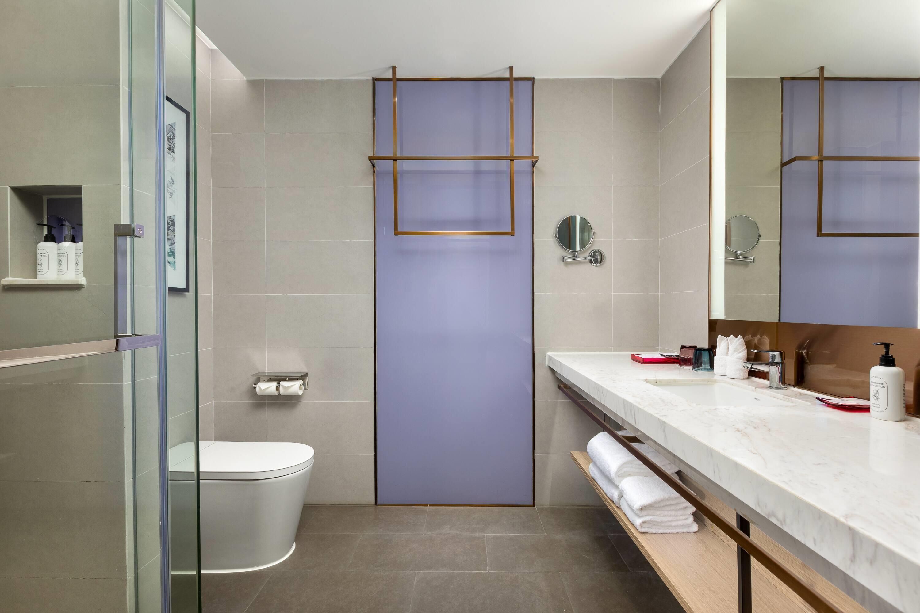 Un baño moderno con cabina de ducha de vidrio, inodoro, lavabo con encimera de mármol y espejo.