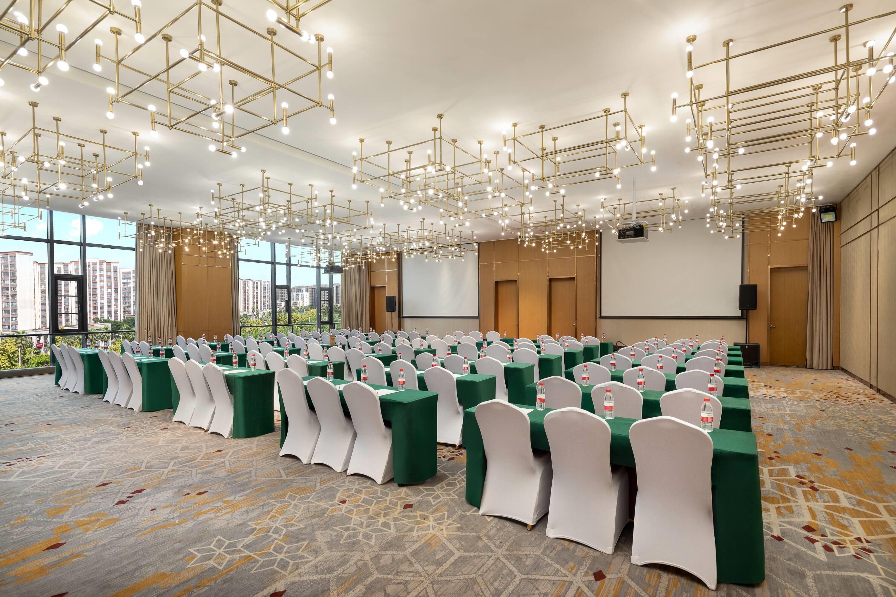 Un salón de conferencias con filas de mesas, sillas blancas y una lámpara de araña moderna.