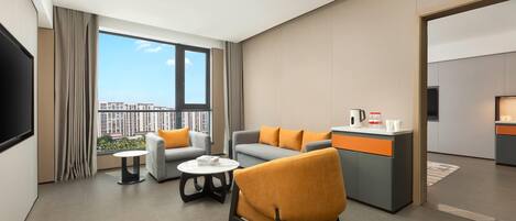 Habitación de hotel moderna con sofá, sillón y mesa de centro. Se aprecia una cocina al fondo.