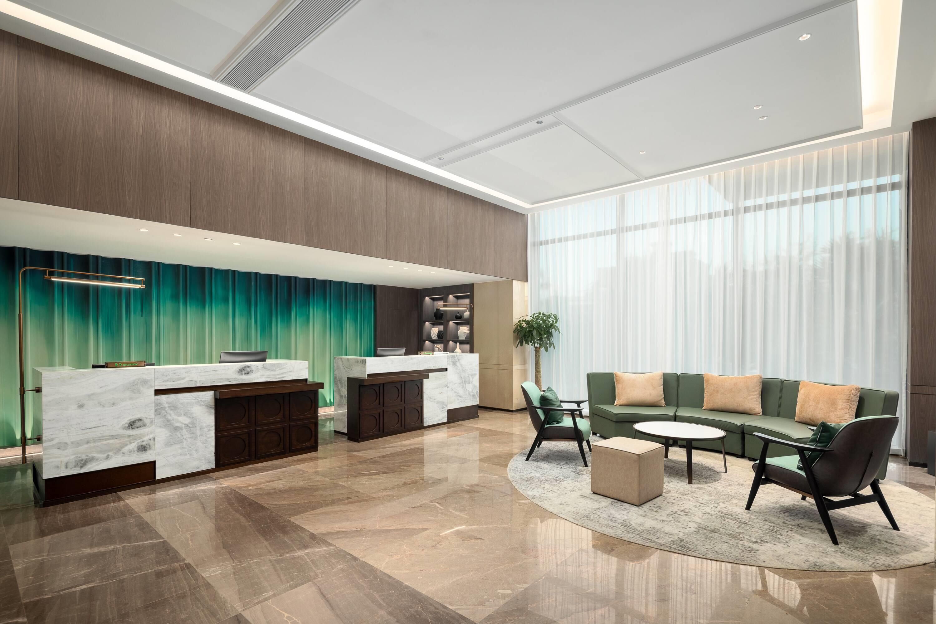 A modern hotel lobby with a reception desk, seating area, and a large window with curtains.