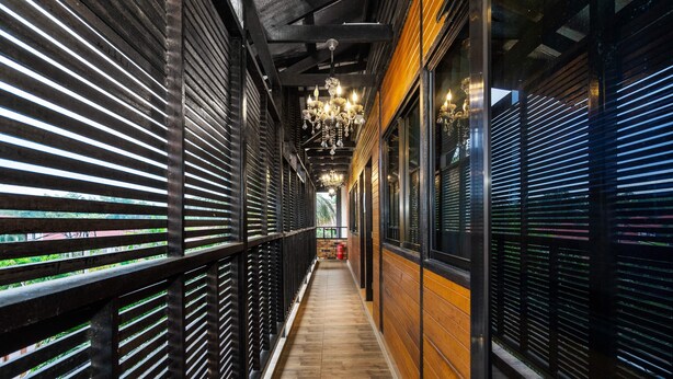 A narrow corridor with wooden flooring, black metal railings, and a row of windows on one side. - Villa Kiambang (Seremban)