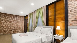 A hotel room with a brick wall, a bed with white bedding, a nightstand with a lamp, and a window with colorful curtains. - Villa Kiambang (Seremban)