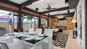 A dining area with a glass table, white wicker chairs, and a brick wall. - Villa Kiambang (Seremban)