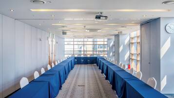 Una sala conferenze con un lungo tavolo, sedie bianche e pavimento rivestito di moquette.