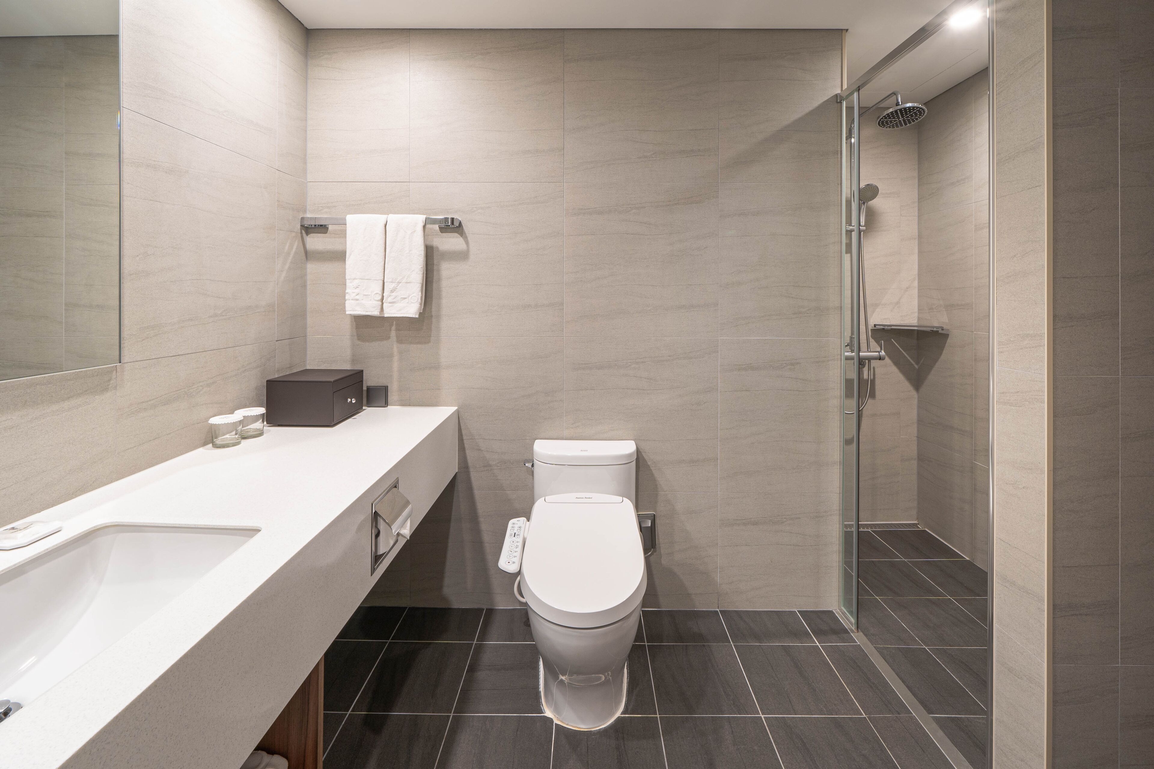 A modern bathroom with a white toilet, a shower, and a large mirror.