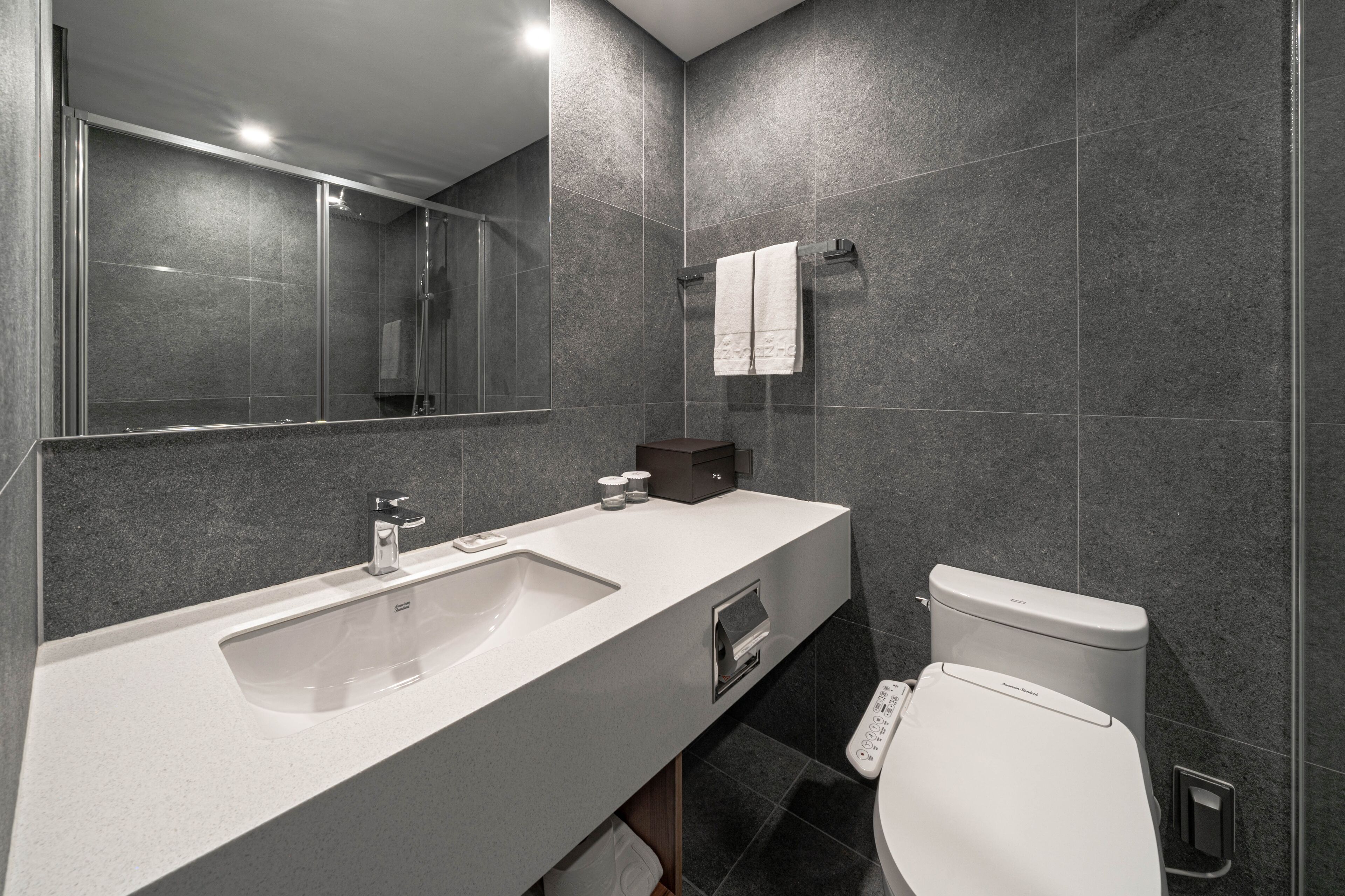 A modern bathroom with a large mirror, a sink, a toilet, and a shower.