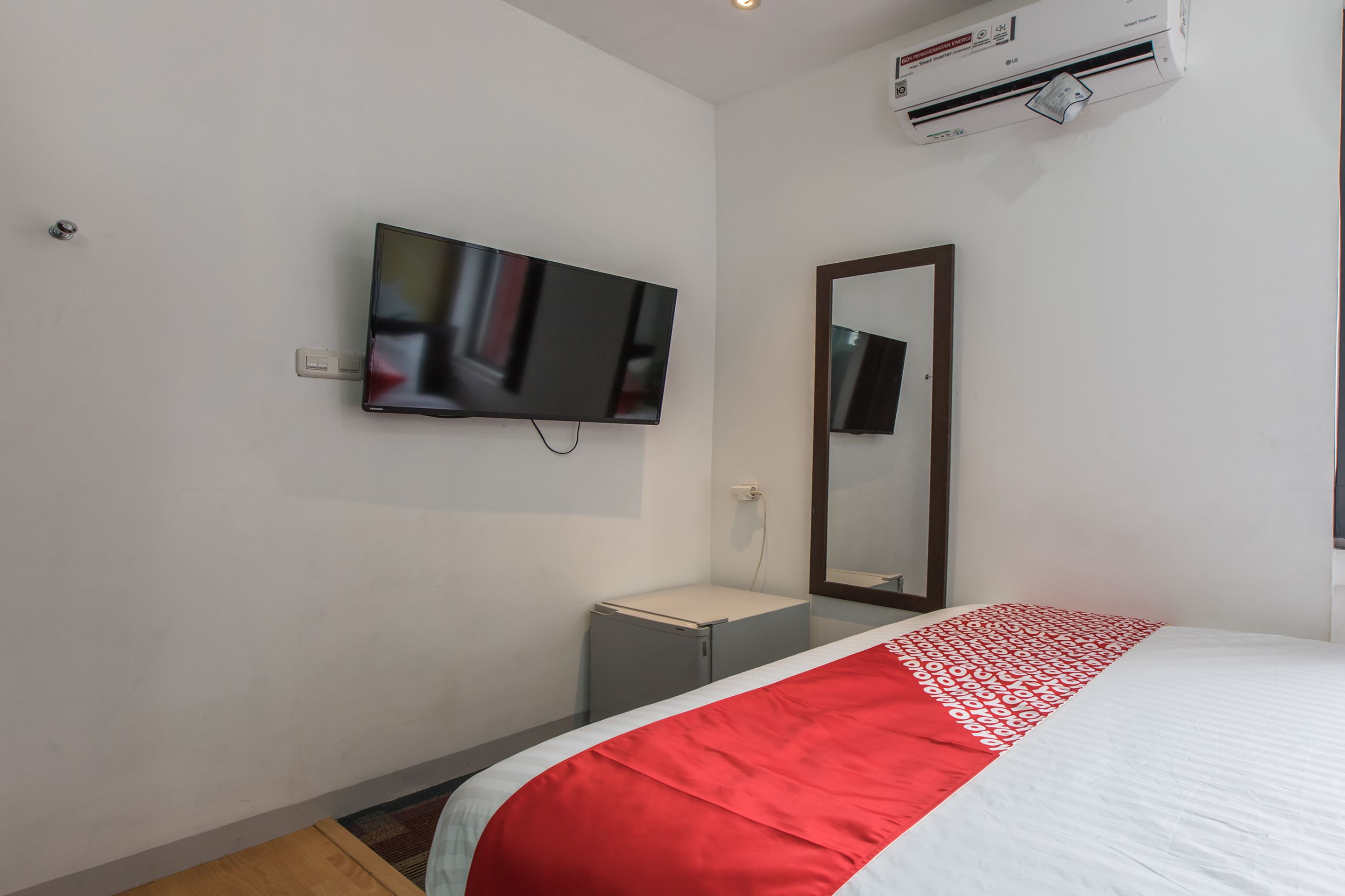 A hotel room with a bed, a TV mounted on the wall, a small bedside table, and a mirror.
