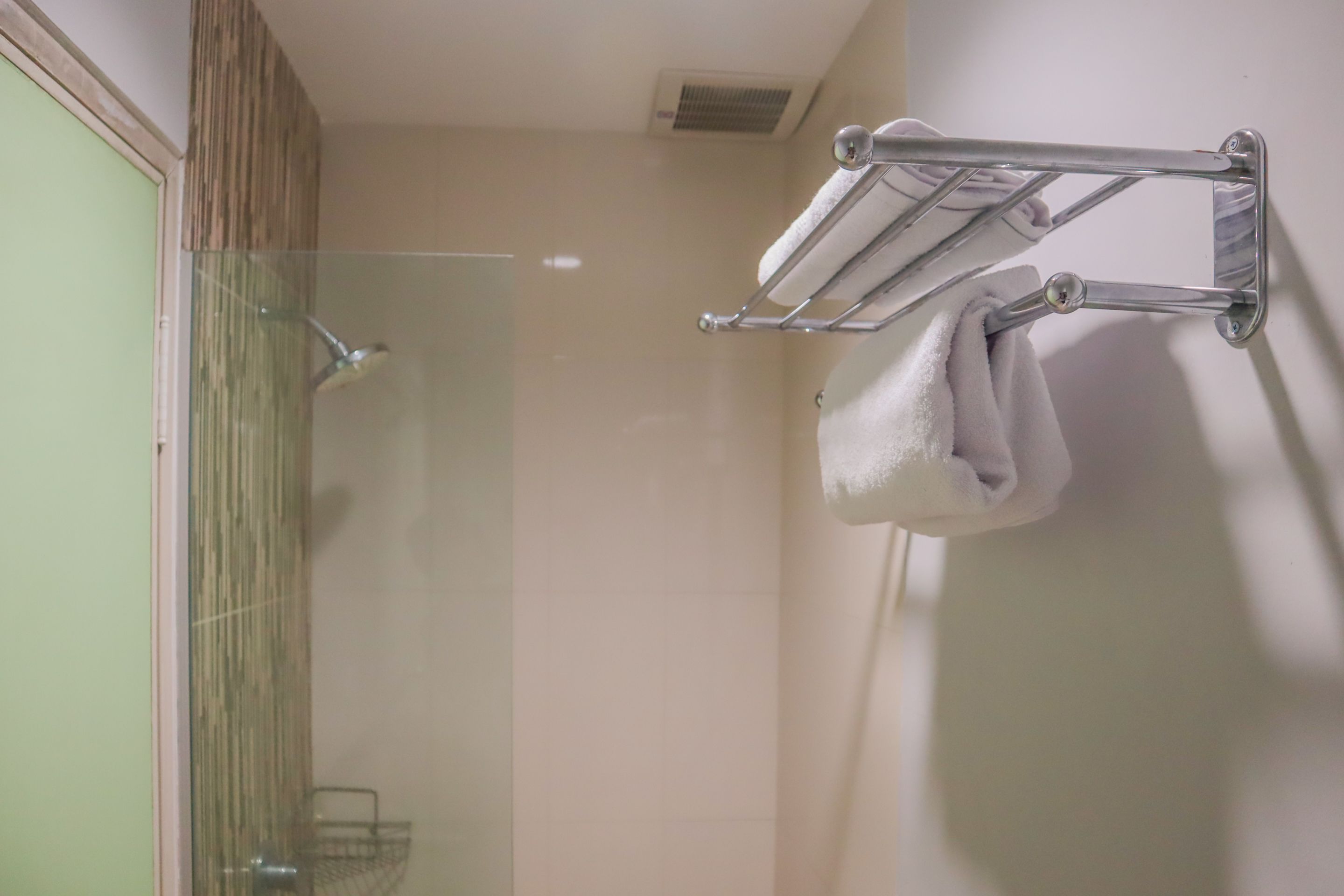 A bathroom with a glass shower enclosure, a towel rack with two towels, and a wooden panel on the left.