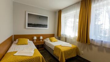 Ein Hotelzimmer mit zwei Betten, einem Nachttisch, einer Lampe, einem gerahmten Bild an der Wand und einem Fenster mit Vorhängen.