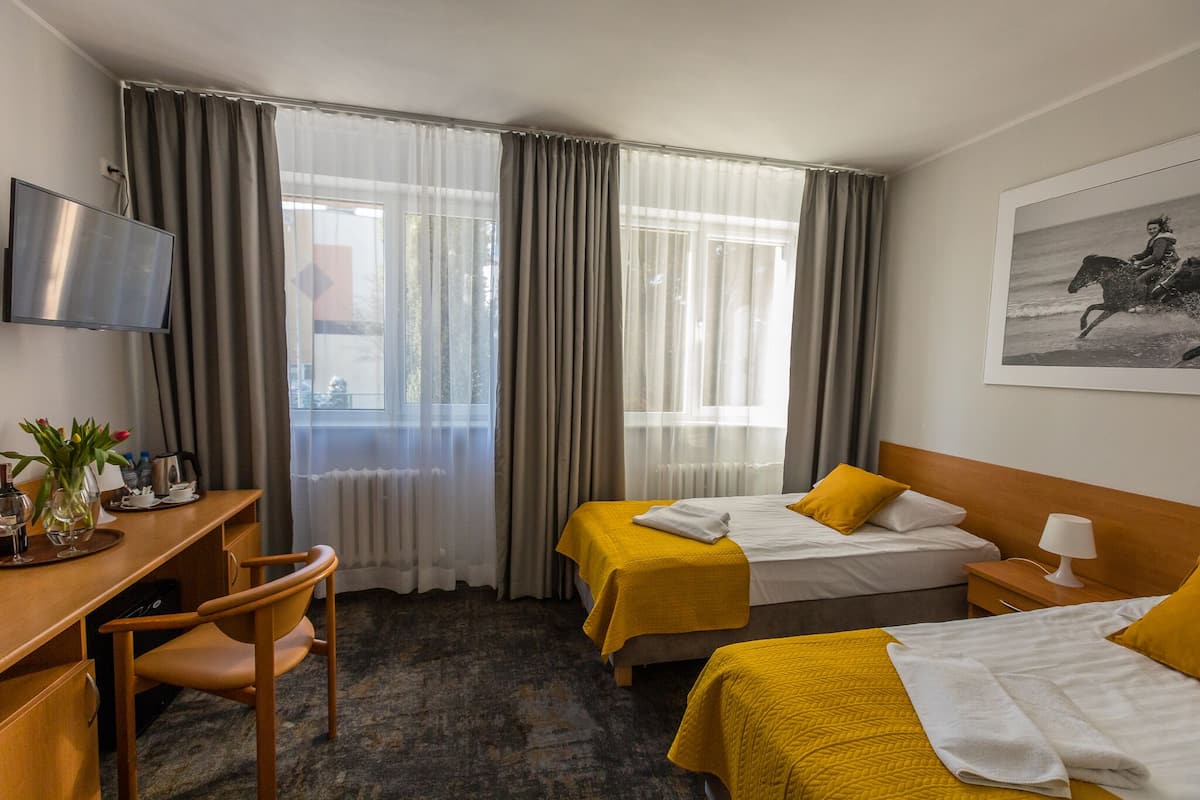 A hotel room with two beds, a desk, a chair, a TV, and a painting on the wall.