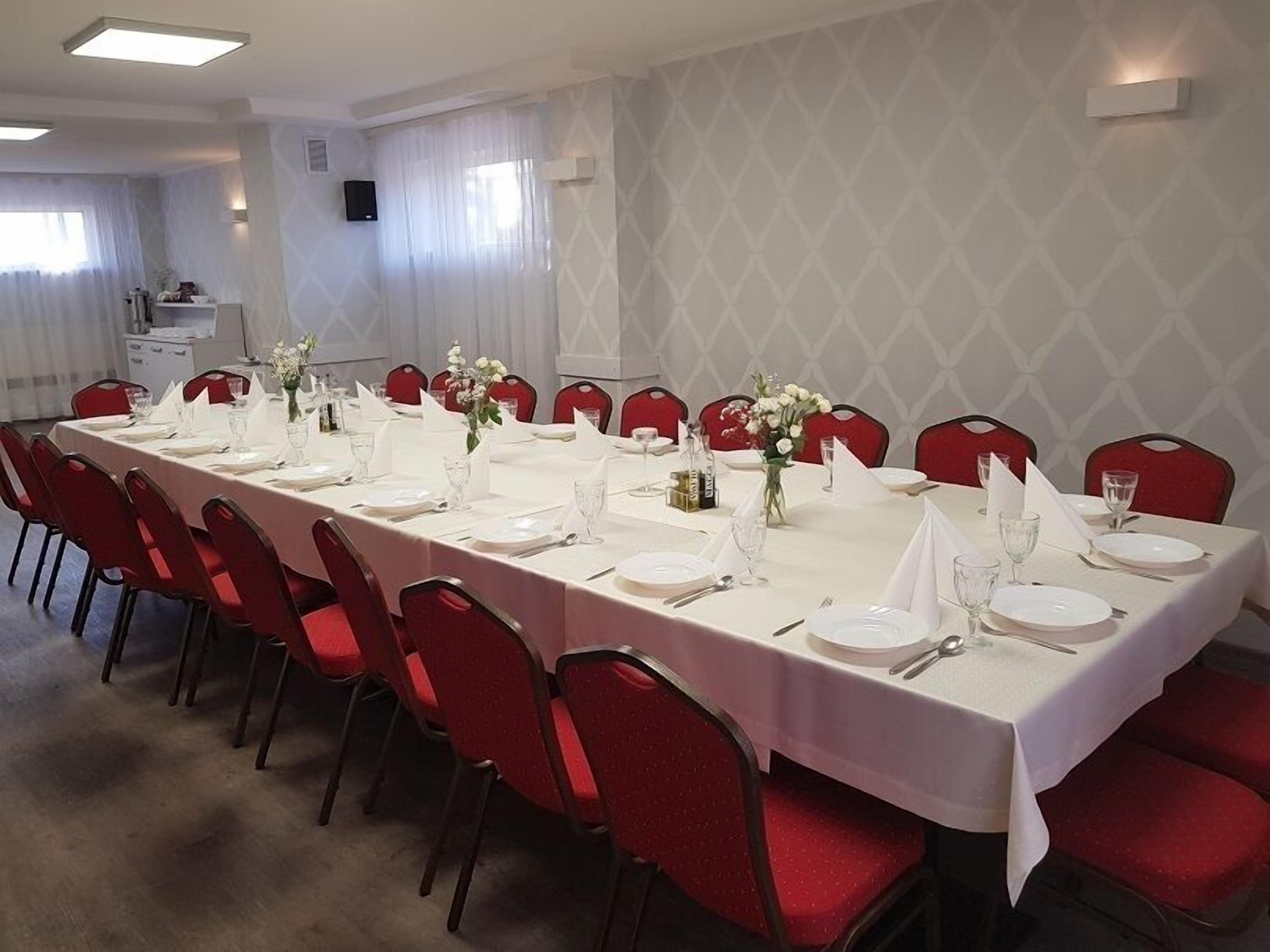 A long dining table set for a formal meal with red chairs, white tablecloth, and floral centerpieces.