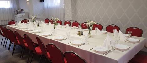 A long dining table set for a formal meal with red chairs, white tablecloth, and floral centerpieces.