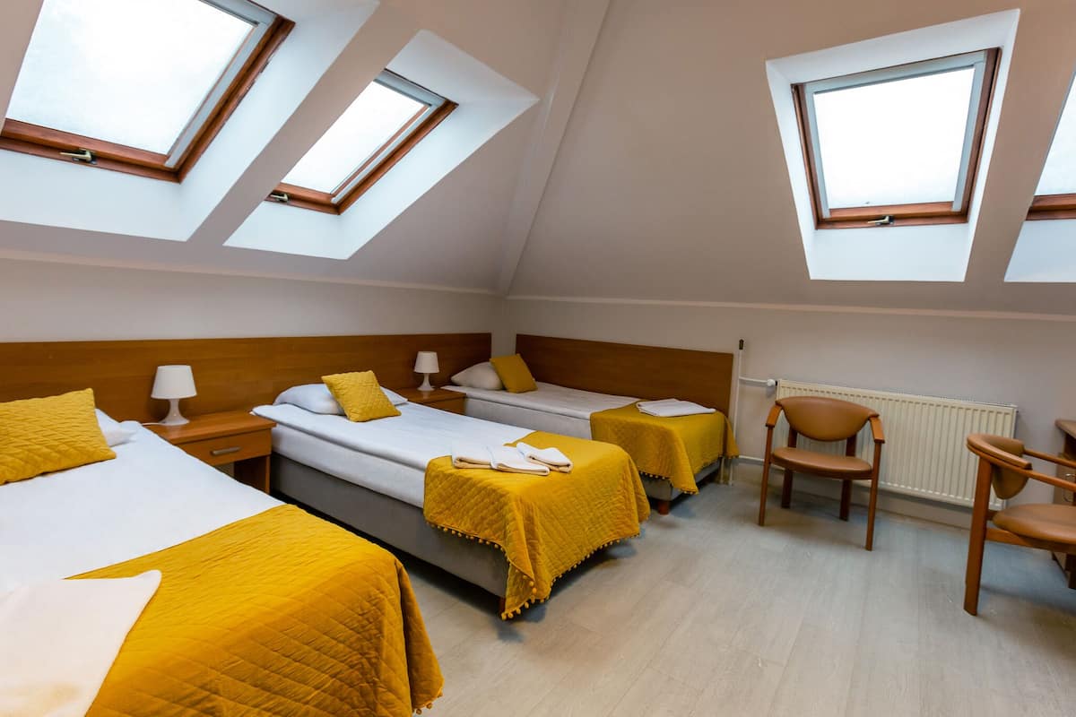 A hotel room with three beds, a desk, and a chair. Each bed has a yellow blanket and white pillows. There are skylights on the ceiling.