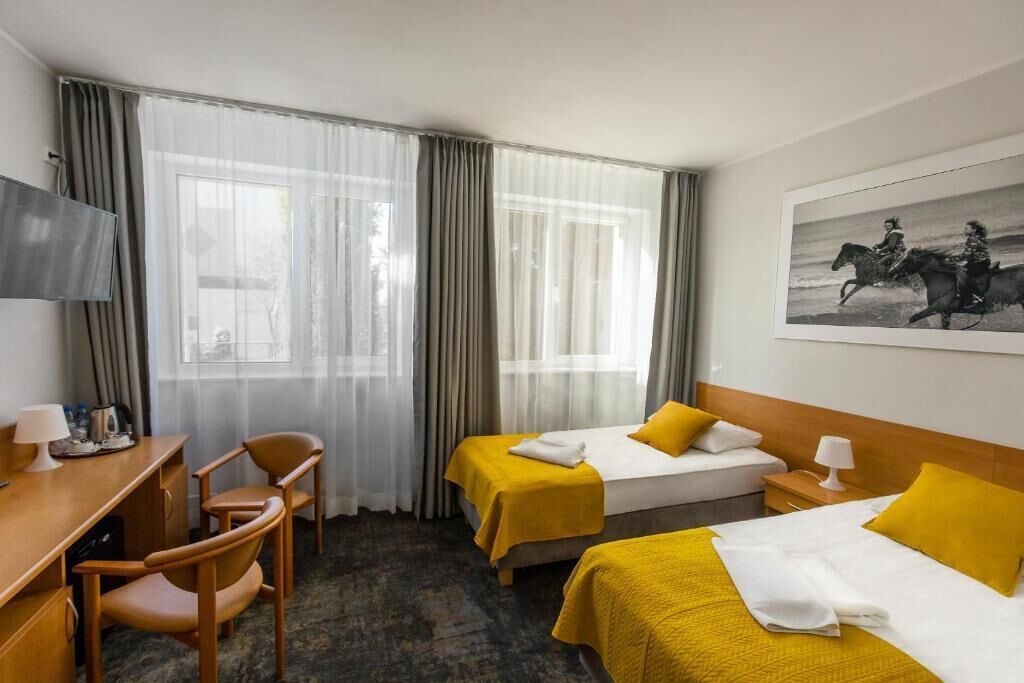 A hotel room with two beds, a desk, chairs, a TV, and a painting on the wall.