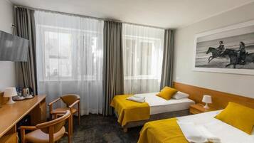A hotel room with two beds, a desk, chairs, a TV, and a painting on the wall.