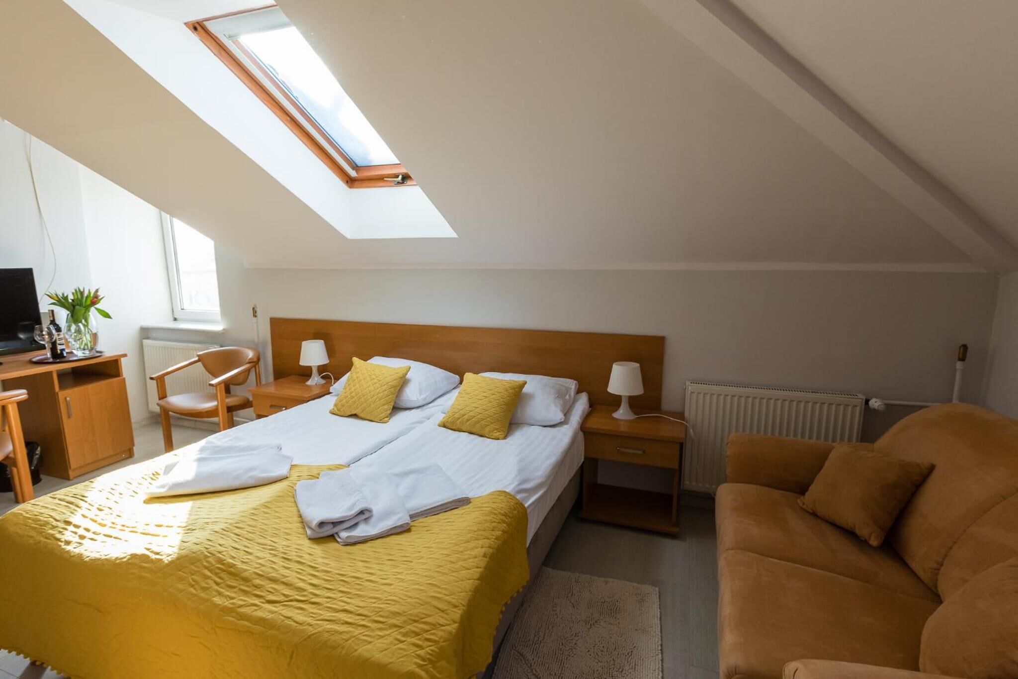 Una habitación de hotel con cama, escritorio, sillón, sofá y tragaluz.