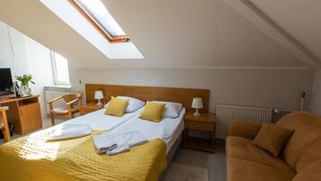 Una habitación de hotel con cama, escritorio, sillón, sofá y tragaluz.