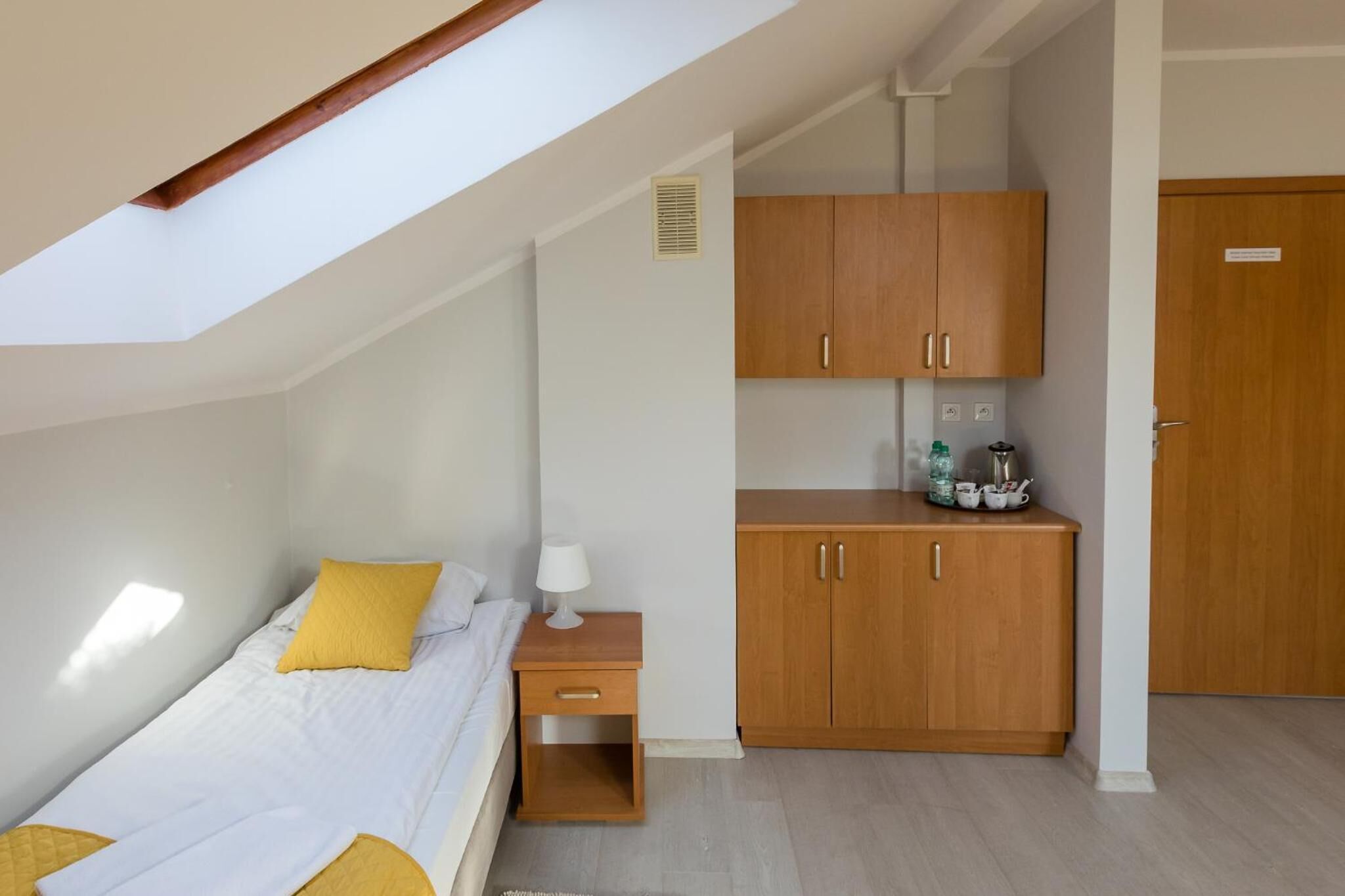 Un dormitorio con cama, mesita de noche, armario de madera y tragaluz.